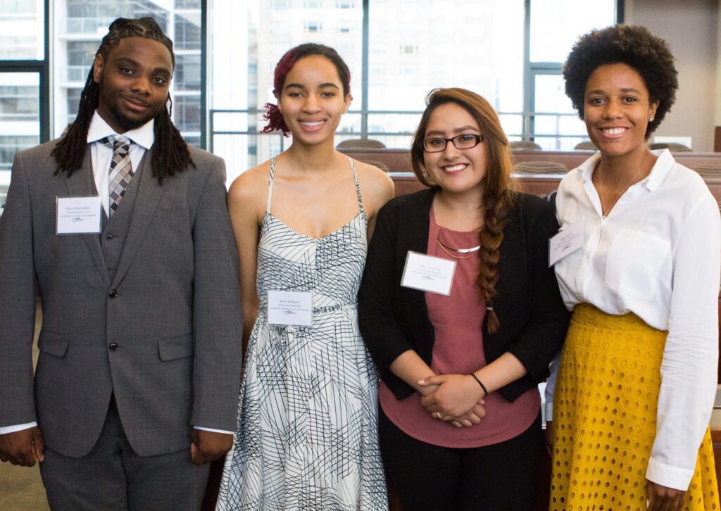 Four young people of color, wearing suits and dresses, smile for camera.