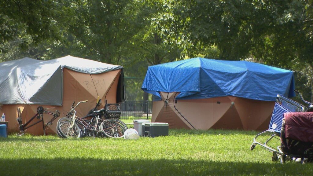 2 large tents covered in tarps in a park. Bikes and other items are around them.