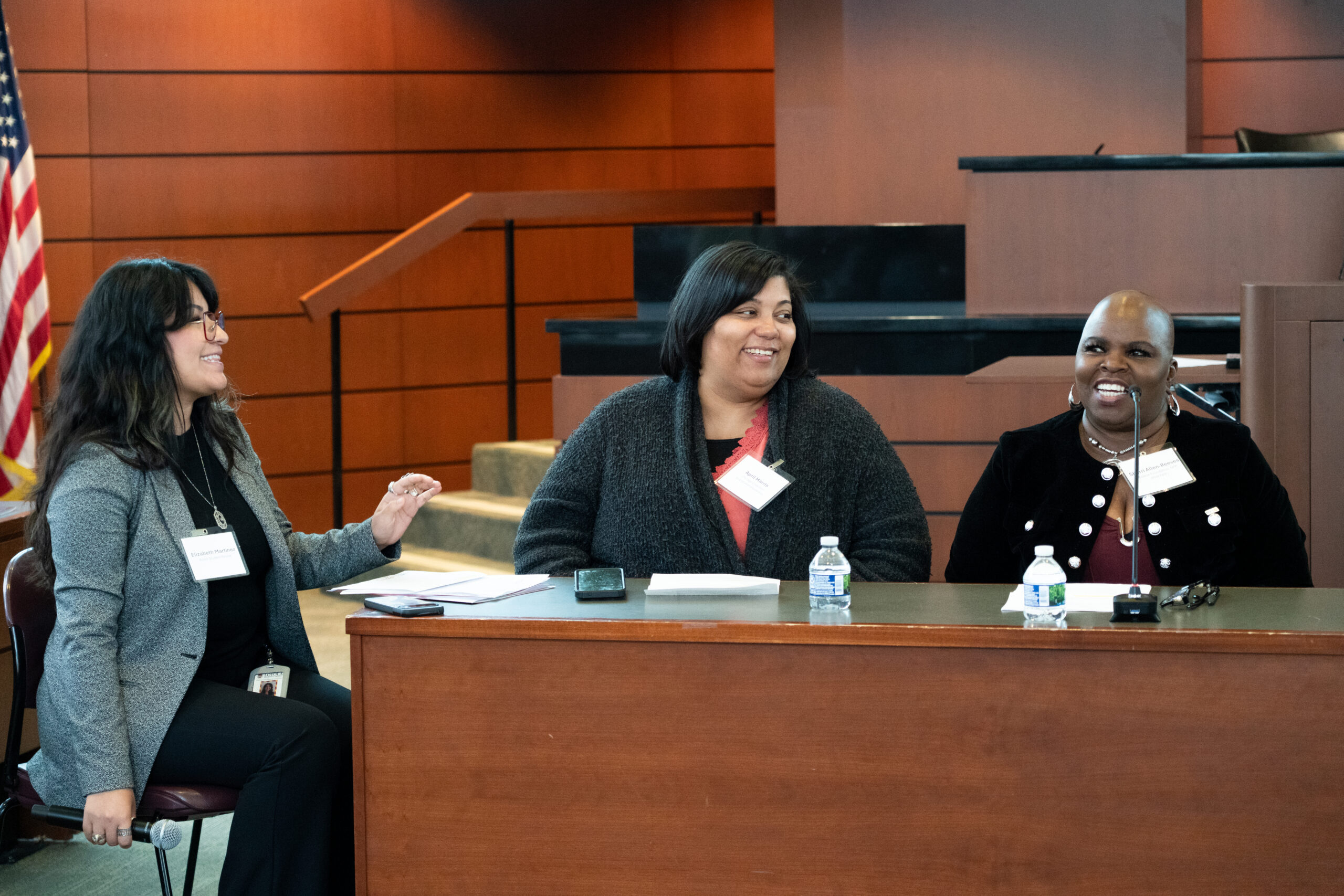 A photography of 3 people smiling, sitting at a table at a symposium panel.