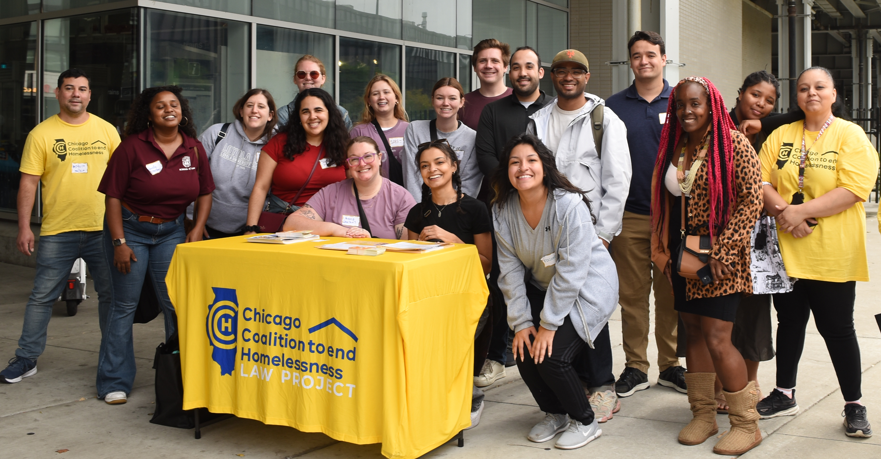 A group of students and CCH staff stand behind a table with a yellow table cloth and the Chicago Coalition to end Homelessness Logo on it.