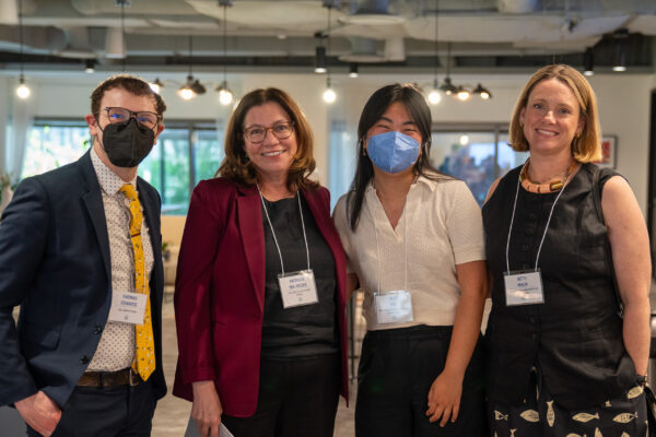 Four people in professional attire pose for the camera. 2 are wearing masks and 2 are smiling.