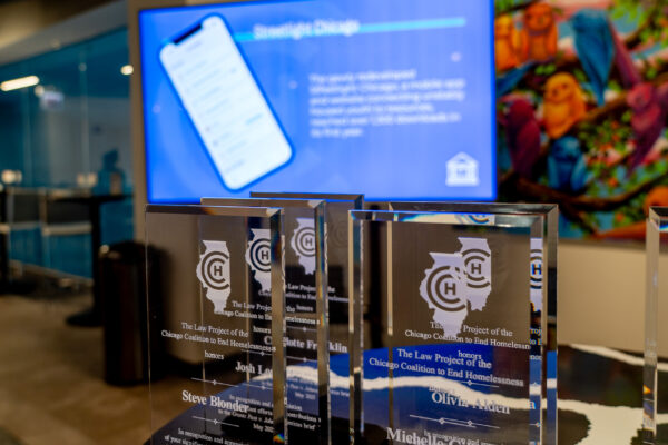 Glass awards with an etched CCH logo are in the foreground with a blue projection screen in the background.