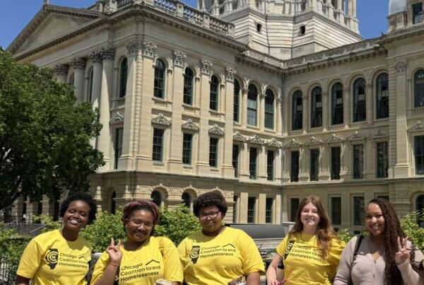 A group of young people in bright yellow shirts stand in front of the Illinois State Capitol building.