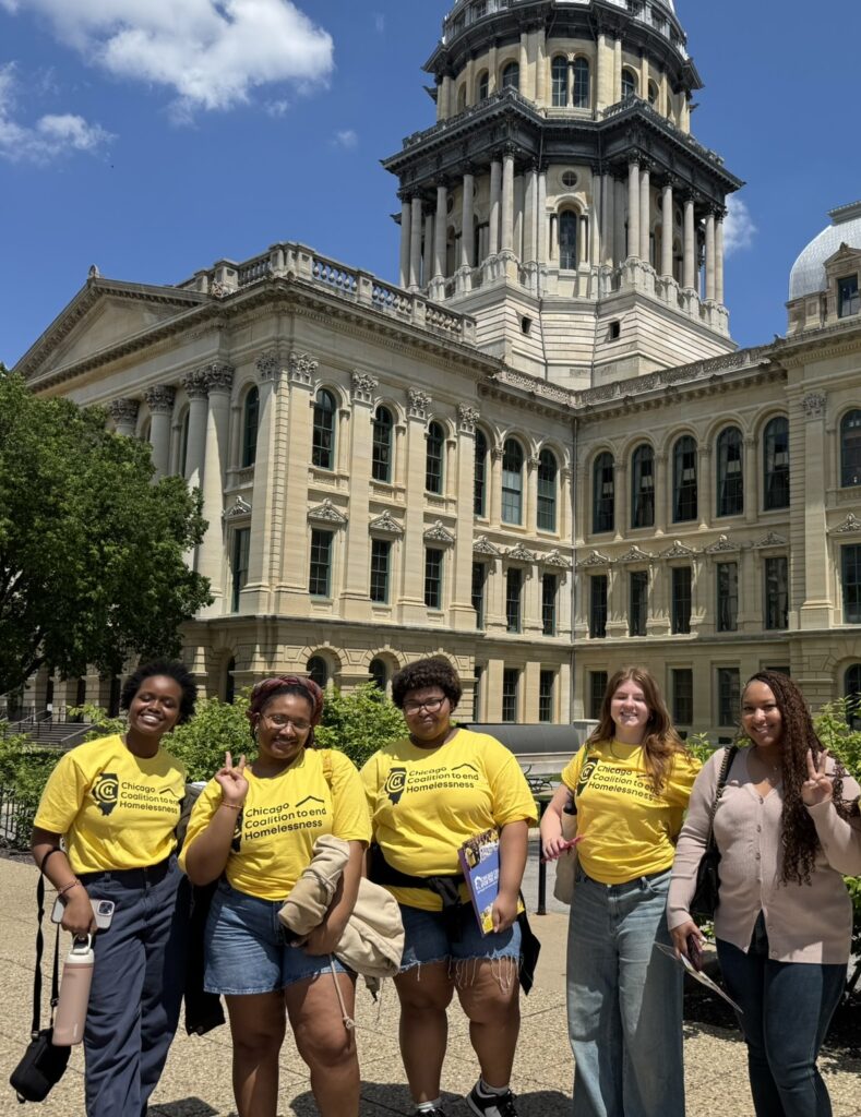 A group of young people in bright yellow shirts stand in front of the Illinois State Capitol building.