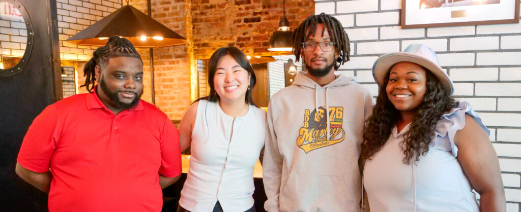 Four people stand, smiling at the camera in a restaurant setting.