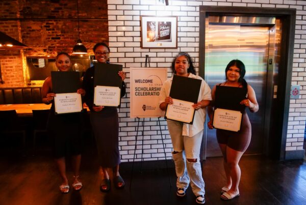 Four young people hold certificates and pose in front of a sign that says 'Welcome to the Scholarship Celebration'