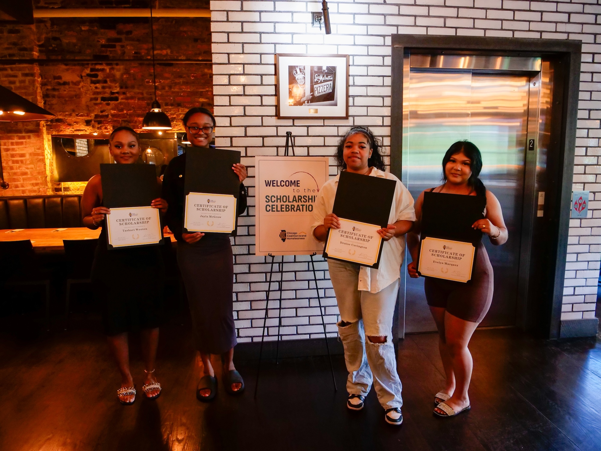 Four young people hold certificates and pose in front of a sign that says 'Welcome to the Scholarship Celebration'