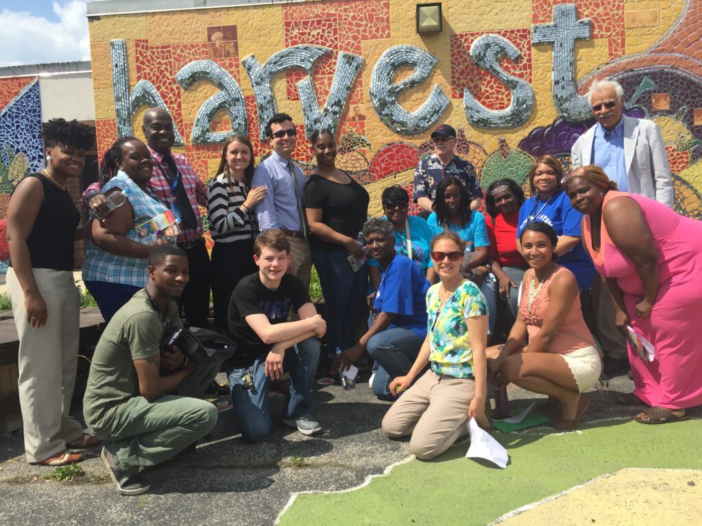 Group of people standing in front of a colorful exterior wall reading "harvest"