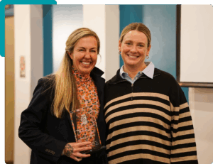 Two people smiling at the camera, one holding a glass award