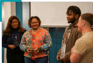 Four people facing each other, three hold glass award plaques, all smiling