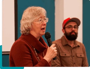 One person speaks into a microphone while another watches from the background