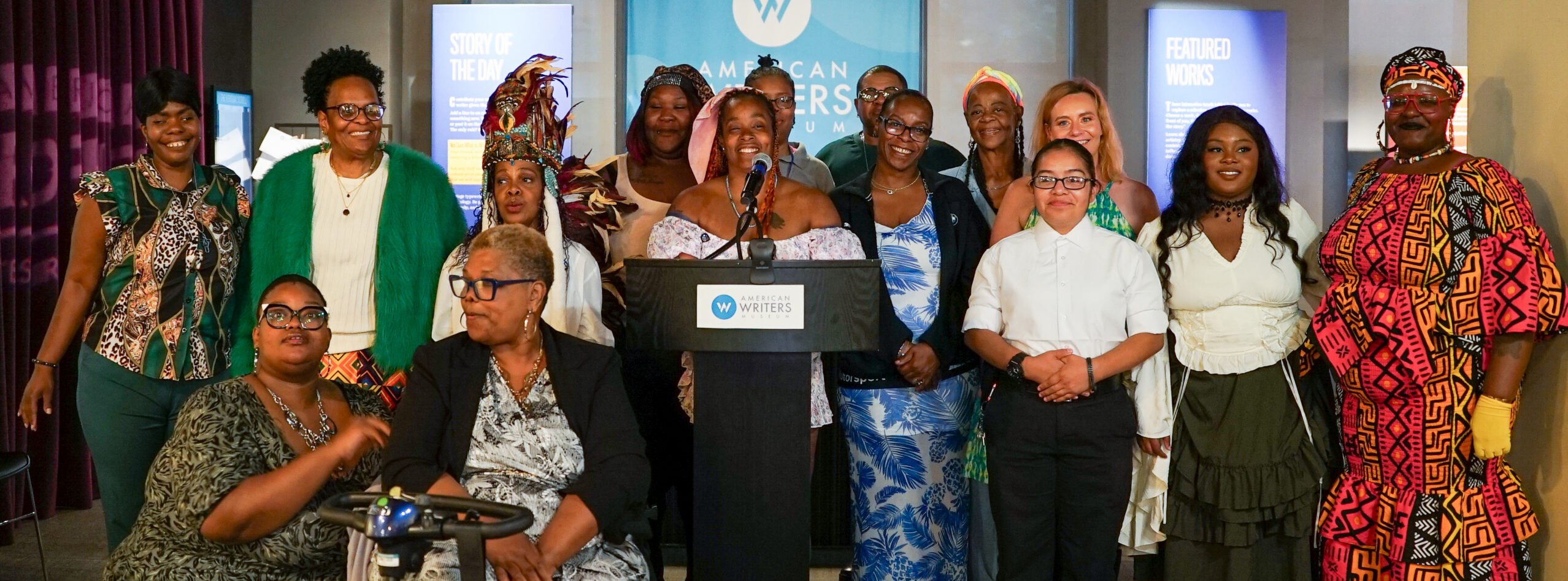 Group of people smiling and posing for the camera in the American Writers Museum behind a podium bearing the Museum's Logo