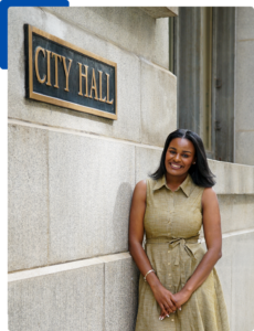 Person smiles at the camera, leaning casually against a building labeled "City Hall"